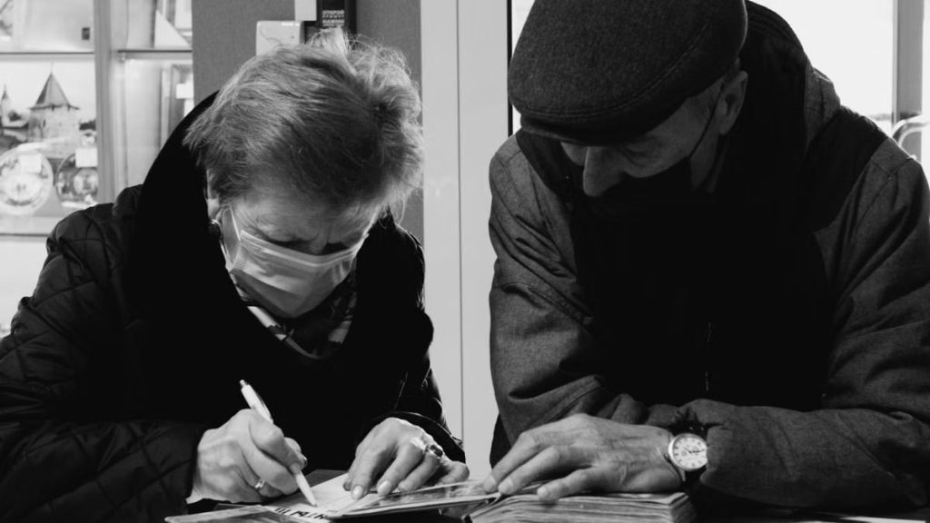 Black and white photo of an elderly couple doing administrative work with face masks.